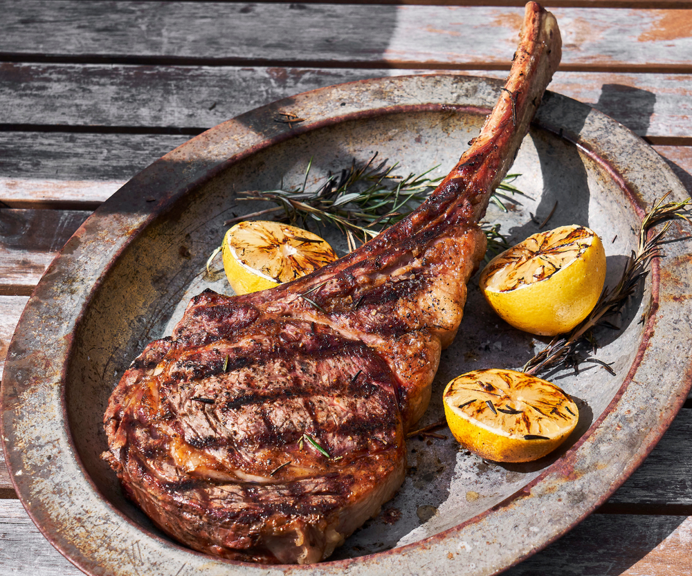 Grilled Tomahawk Ribeye on a plate with charred lemon wedges and rosemary around it