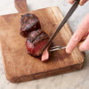 A person slicing a cooked filet mignon on a wooden cutting board.