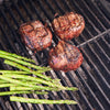 Three 6 oz. cooked filet mignons on a grill next to asparagus.